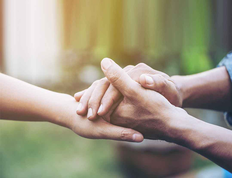 Zwei Hände halten sich fest, die sanft von einer weiteren Hand gestützt werden. Das Bild symbolisiert Solidarität, Unterstützung und Partnerschaft im Rahmen von humanitären Projekten oder strategischen Kooperationen.