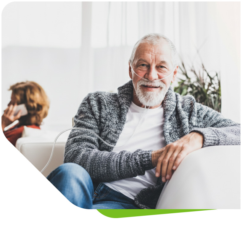 Ein lächelnder, älterer Herr sitzt entspannt auf einem Sofa und liest ein Buch. Er trägt eine Nasenbrille, die die Sauerstofftherapie von VIVISOL dezent in seinen Alltag integriert und seine Lebensqualität verbessert.